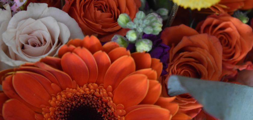 Vibrant arrangement of orange gerbera daisies, roses, and pastel blooms showcasing beauty.