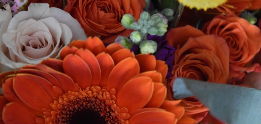 Vibrant arrangement of orange gerbera daisies, roses, and pastel blooms showcasing beauty.