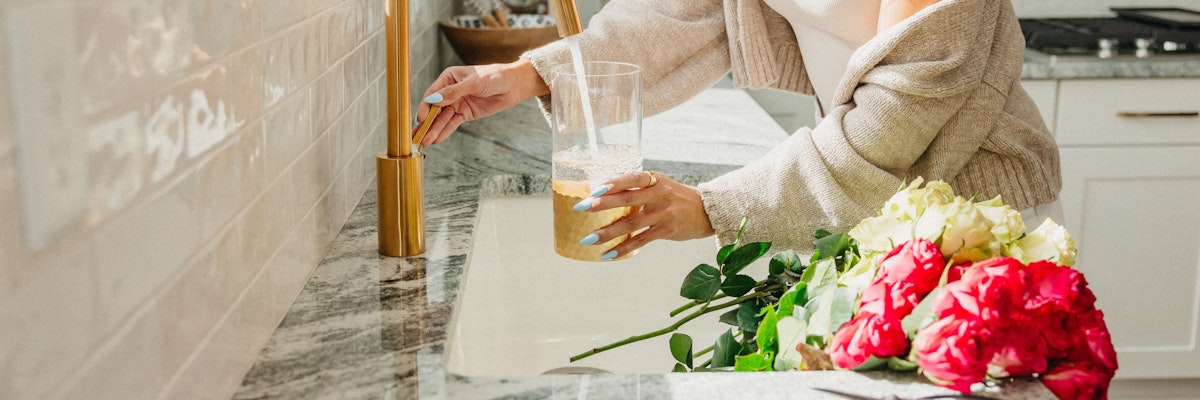 A woman in a cozy kitchen filling a glass with juice beside vibrant pink and white roses.