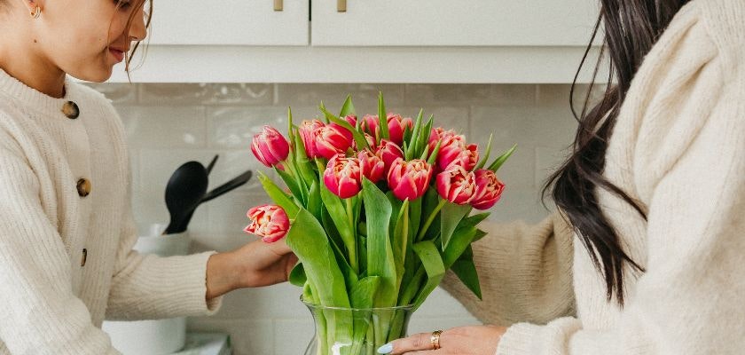 Two women arranging a vibrant bouquet of pink and white tulips in a clear vase.