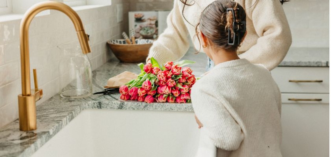 A woman and child arranging vibrant pink tulips on a beautiful kitchen countertop.