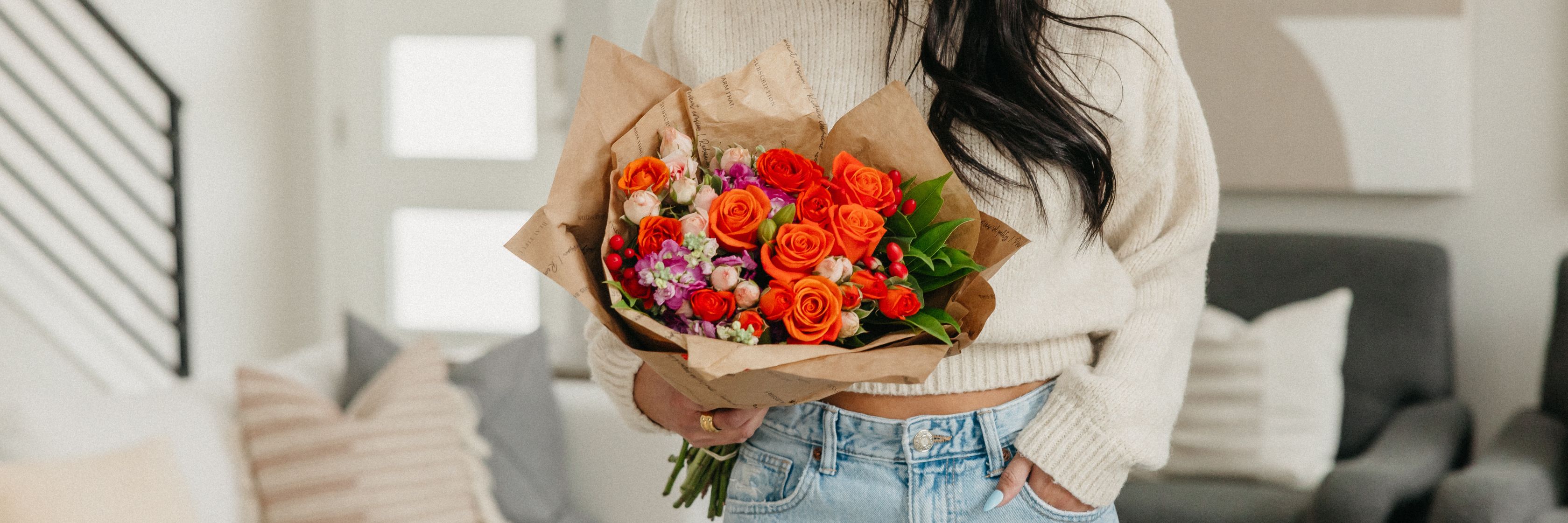 Vibrant bouquet of orange roses and colorful flowers held by a stylish individual indoors.