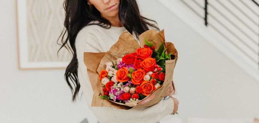 A vibrant bouquet featuring orange roses and colorful mixed blooms, beautifully wrapped.