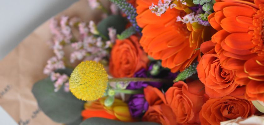 Vibrant floral bouquet featuring orange gerbera daisies, roses, and lavender accents.
