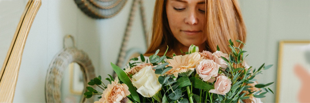 A woman holds a lush bouquet featuring soft pink roses and greenery, radiating warmth.