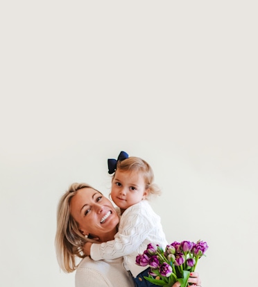 A joyful mother and daughter share a sweet moment while holding a bouquet of purple tulips.