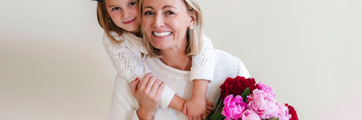 A joyful woman and girl embracing, holding a vibrant flower bouquet together.