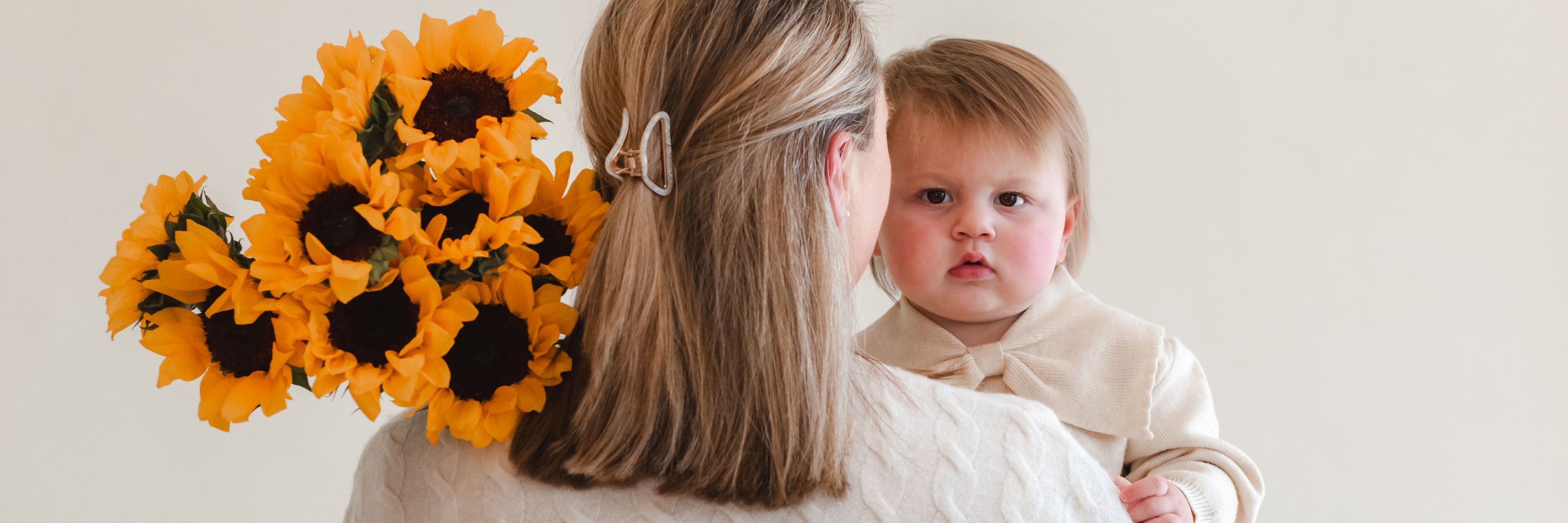 A mother holding her child while carrying a vibrant bouquet of sunflowers.
