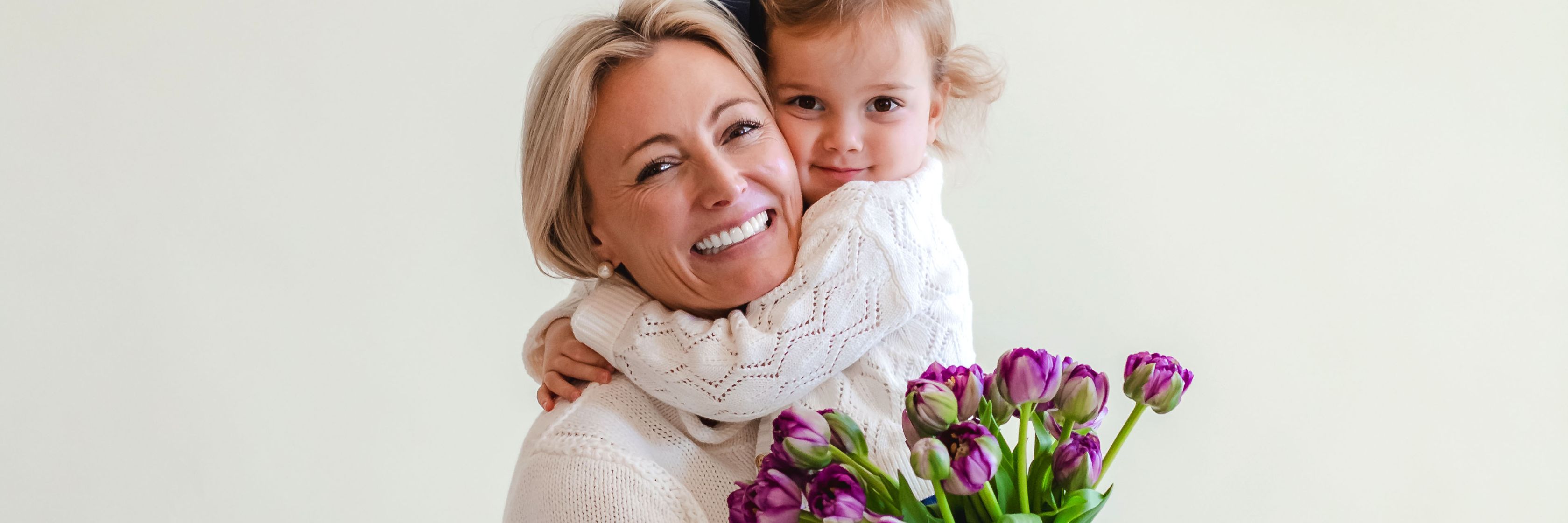 Joyful moment of a mother and daughter smiling, embracing with a bouquet of purple tulips.
