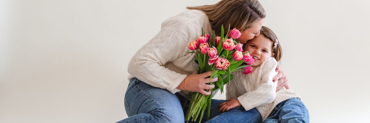 A joyful moment between a mother and daughter, embracing with pink tulips in hand.