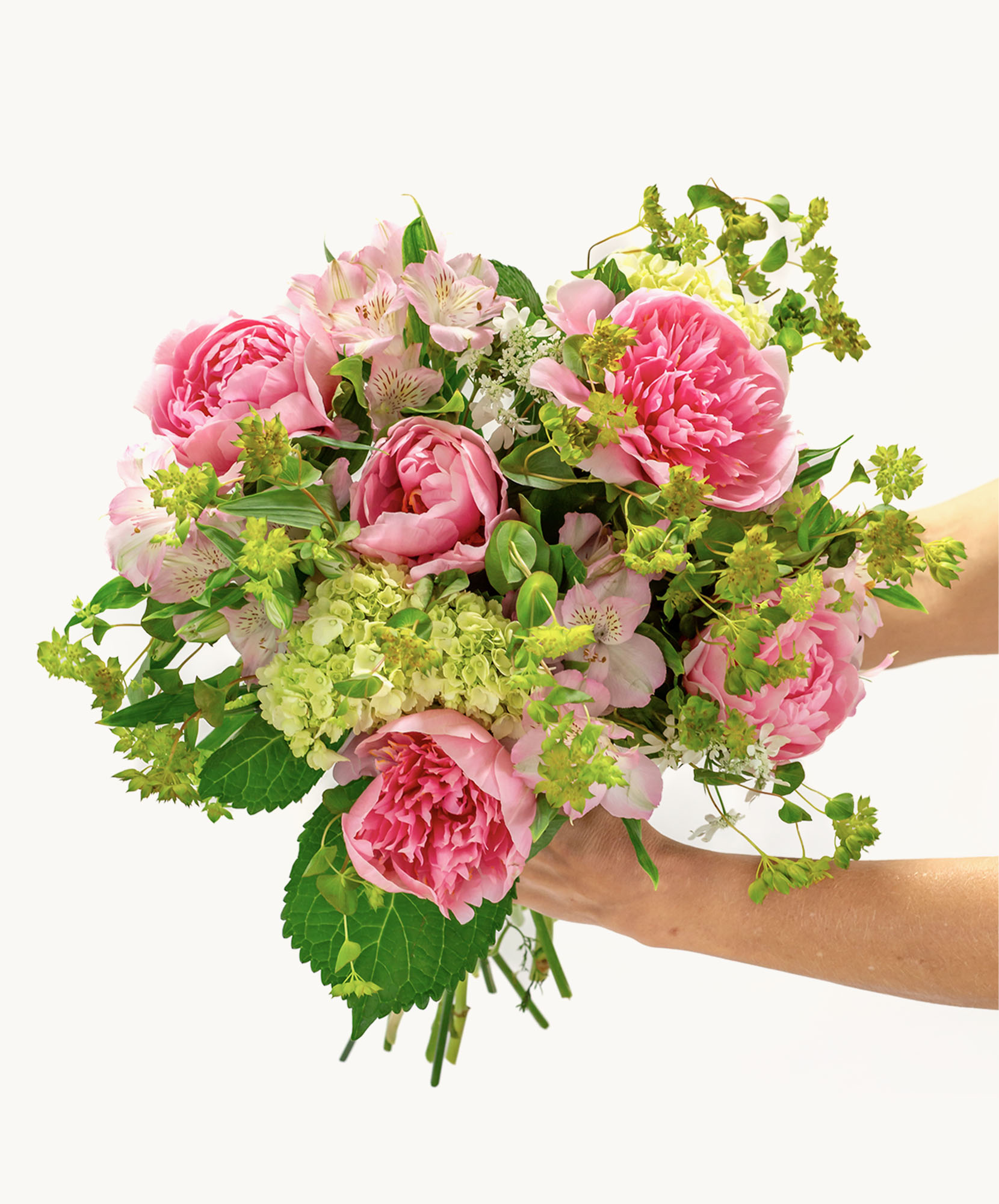 A lush bouquet featuring pink peonies, alstroemeria, and fresh greenery, elegantly held.