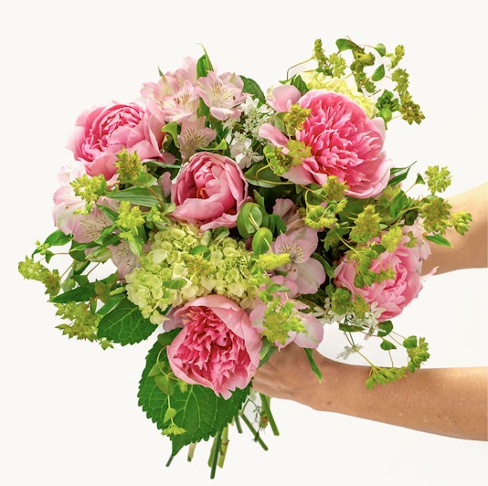 A lush bouquet featuring pink peonies, alstroemeria, and fresh greenery, elegantly held.