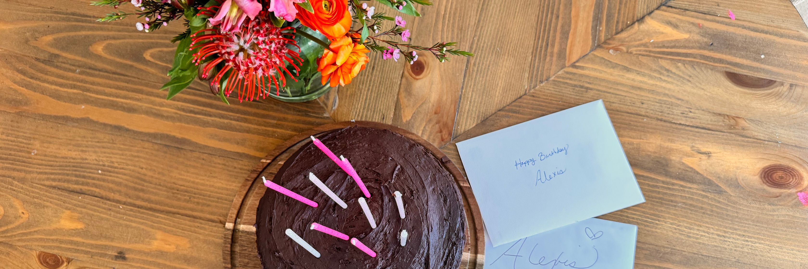 A delicious chocolate birthday cake with candles, surrounded by a vibrant floral bouquet.