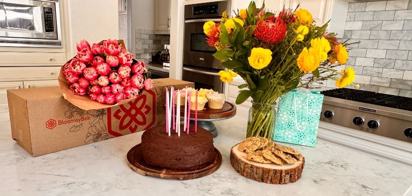 Colorful birthday celebration setup featuring a cake, flowers, and treats on a table.