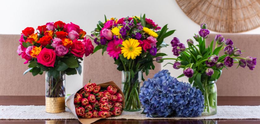 Vibrant floral arrangements featuring roses, tulips, and daisies in elegant vases on a table.