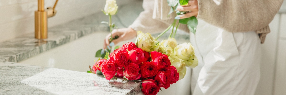 A person arranging vibrant red and white roses on a kitchen countertop, creating a fresh floral display.