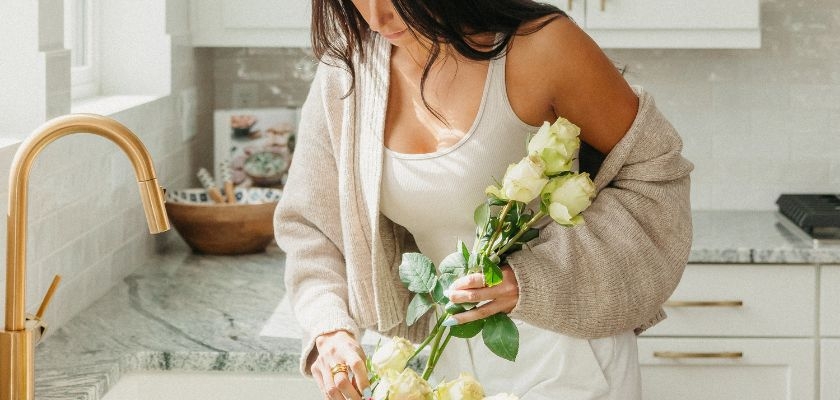 A woman arranging beautiful white roses in a cozy kitchen setting, showcasing elegance.