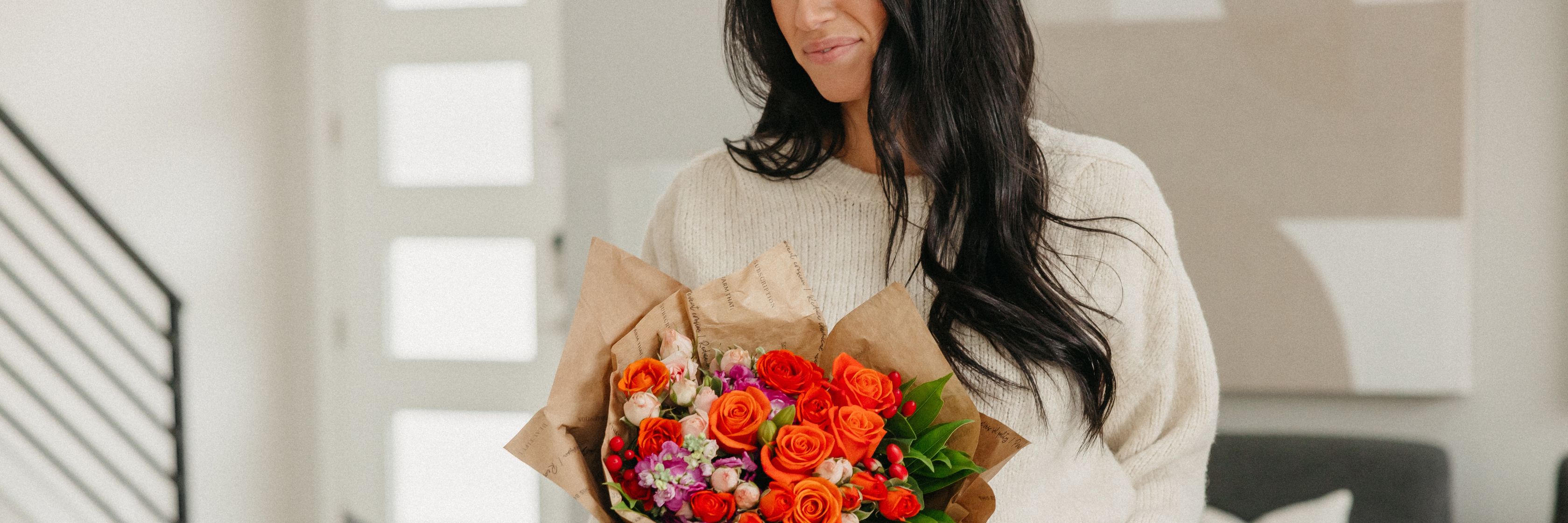A woman holding a vibrant bouquet of orange roses and colorful flowers, radiating joy.