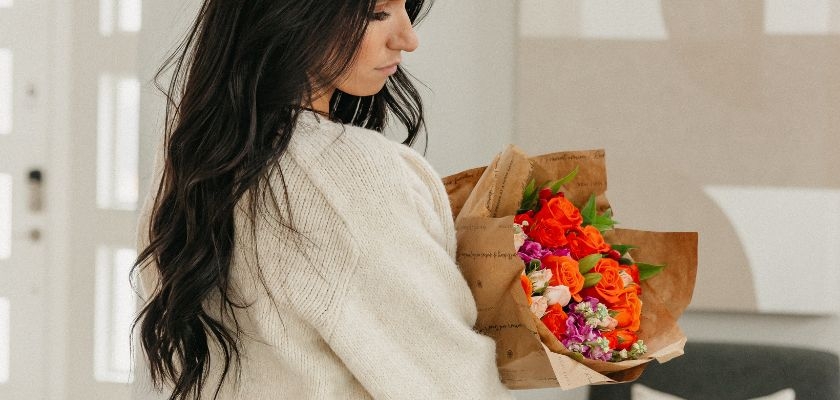 Woman holding a vibrant bouquet of orange and pink roses, perfect for any celebration.