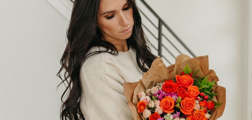 A woman holds a vibrant bouquet of orange roses and assorted blooms in her arms.
