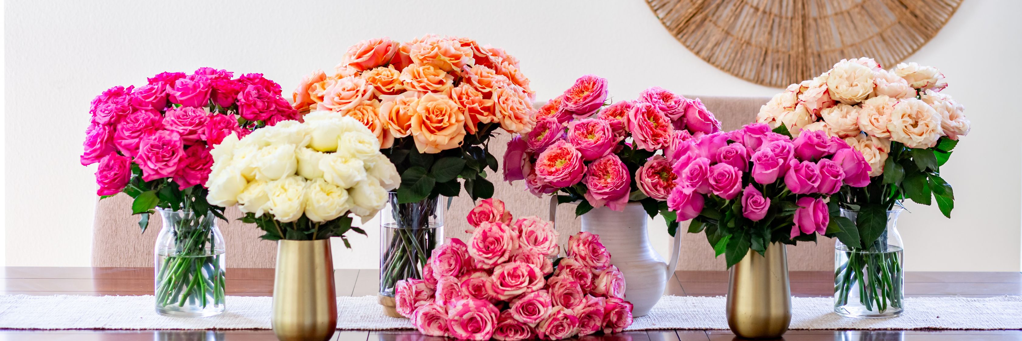Vibrant floral display of pink and peach roses in elegant vases on a dining table.