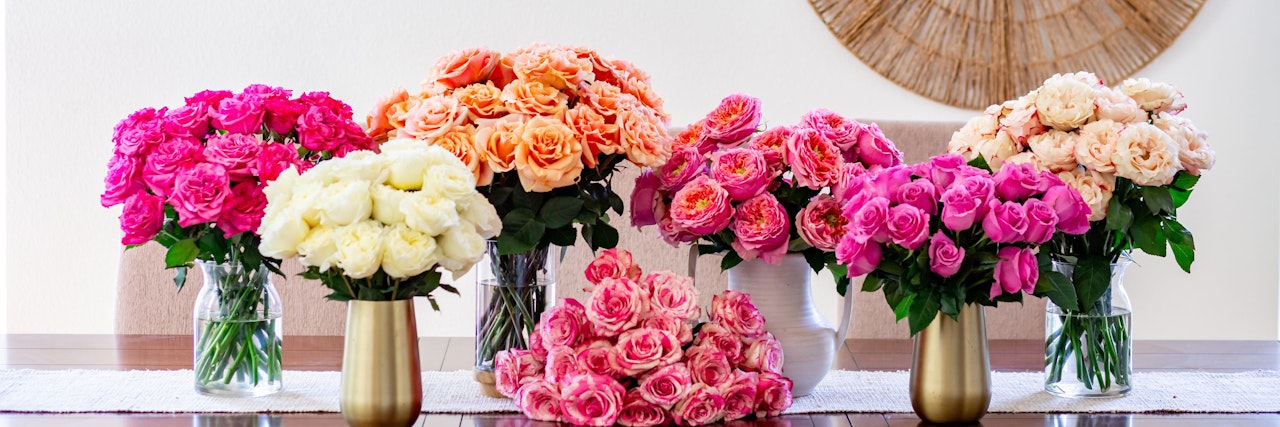 Vibrant floral display of pink and peach roses in elegant vases on a dining table.
