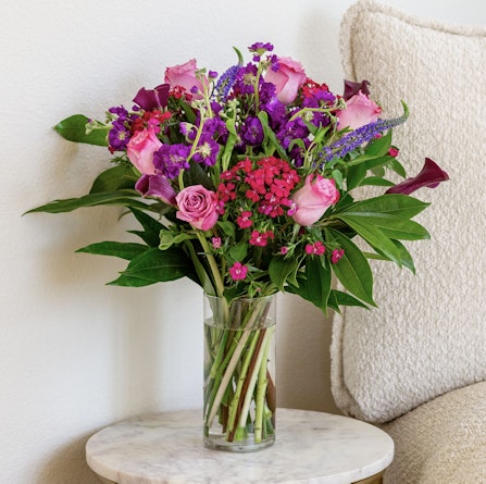 Vibrant floral arrangement with pink roses and purple blossoms in a clear vase.
