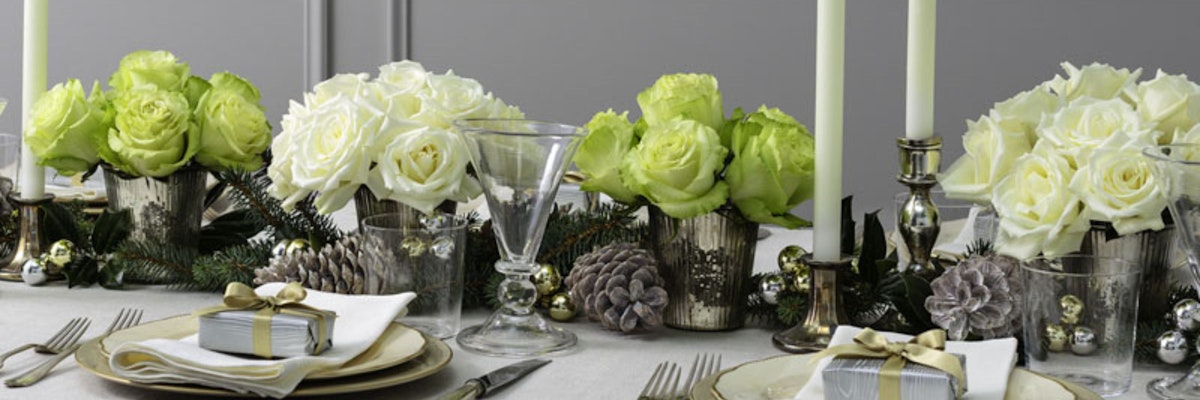 Elegant table setting with white and green roses, pinecones, and candles, perfect for gatherings.
