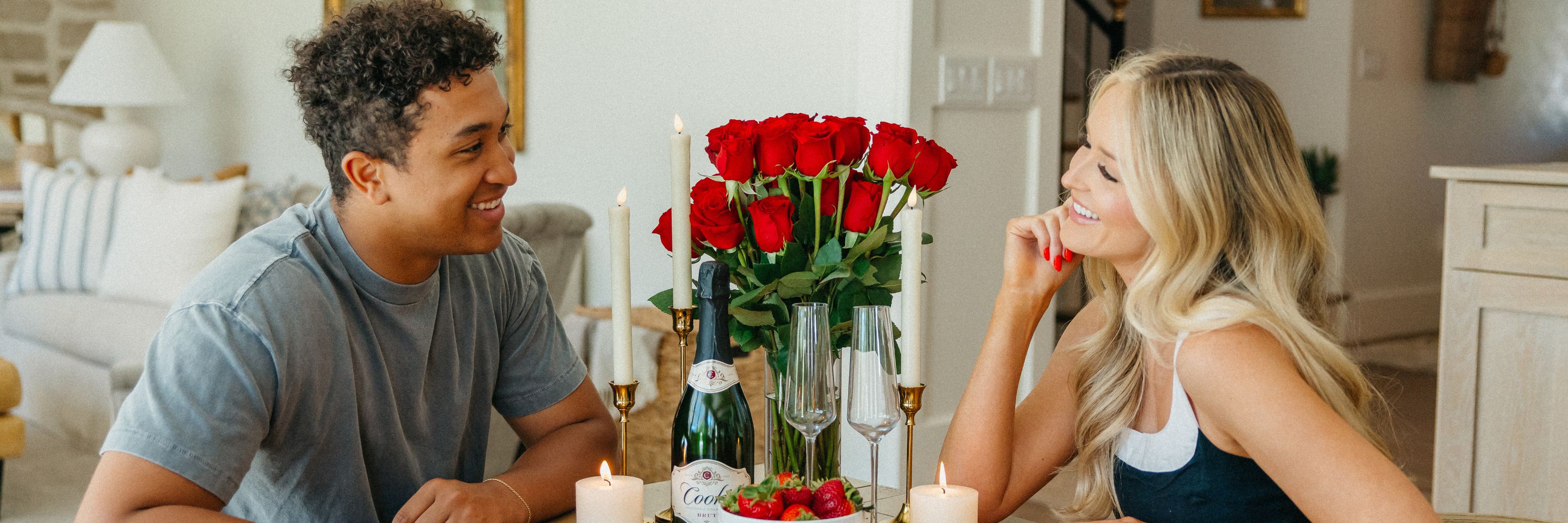 A romantic dining setting with red roses, sparkling wine, and candles for a special celebration.