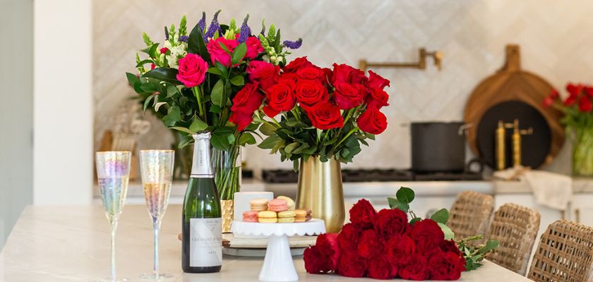 Elegant floral display featuring red roses, champagne, and sweets for a celebration.