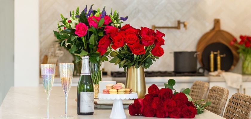 Elegant floral display featuring red roses, champagne, and sweets for a celebration.