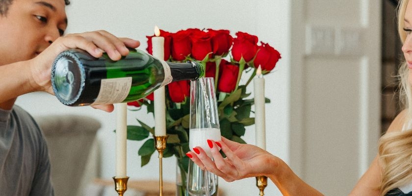 A couple celebrating with a romantic setup featuring red roses and champagne glasses.