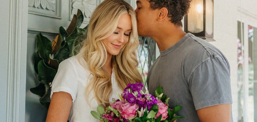A couple shares a sweet moment, with a vibrant bouquet of flowers in her hands.