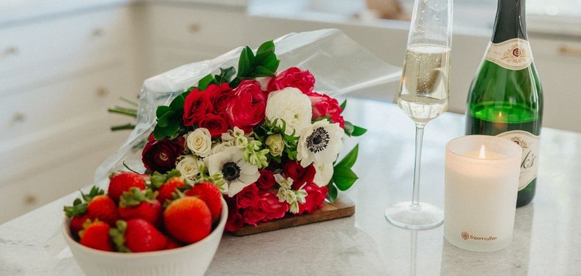 Vibrant bouquet of red and white flowers alongside fresh strawberries and champagne.