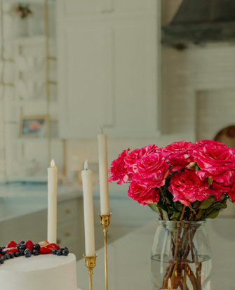 Vibrant pink roses in a glass vase alongside candles and a cake, creating a festive ambiance.