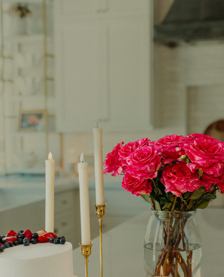 Vibrant pink roses in a glass vase alongside candles and a cake, creating a festive ambiance.