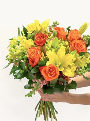 Vibrant bouquet featuring orange roses, yellow lilies, and lush greenery, perfect for celebrations.