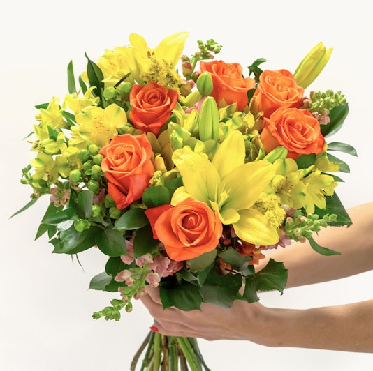 Vibrant bouquet featuring orange roses, yellow lilies, and lush greenery, perfect for celebrations.