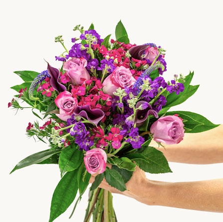 Vibrant bouquet featuring pink roses, purple blooms, and lush greenery, elegantly arranged.