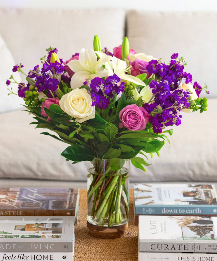 Vibrant floral arrangement with lilies, roses, and purple blooms in a glass vase.