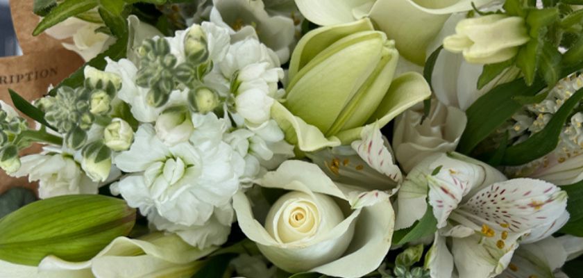 Delicate floral arrangement featuring white roses, lilies, and lush greenery in a charming bouquet.