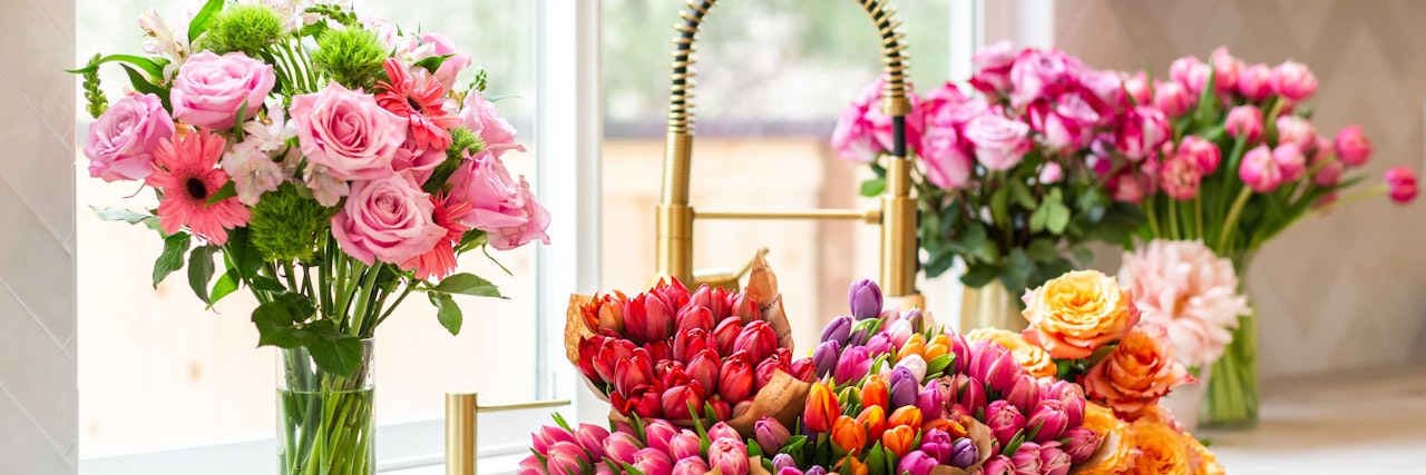 Vibrant floral display featuring pink roses, tulips, and cheerful blooms in a sunny kitchen.