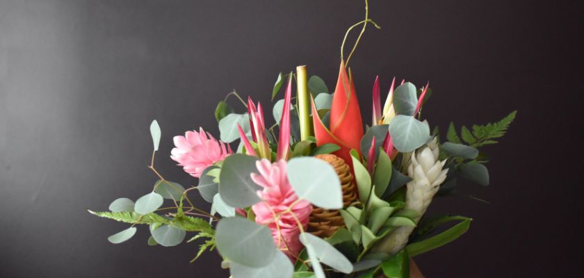 Vibrant tropical flower arrangement featuring pink and red blooms with lush green foliage.