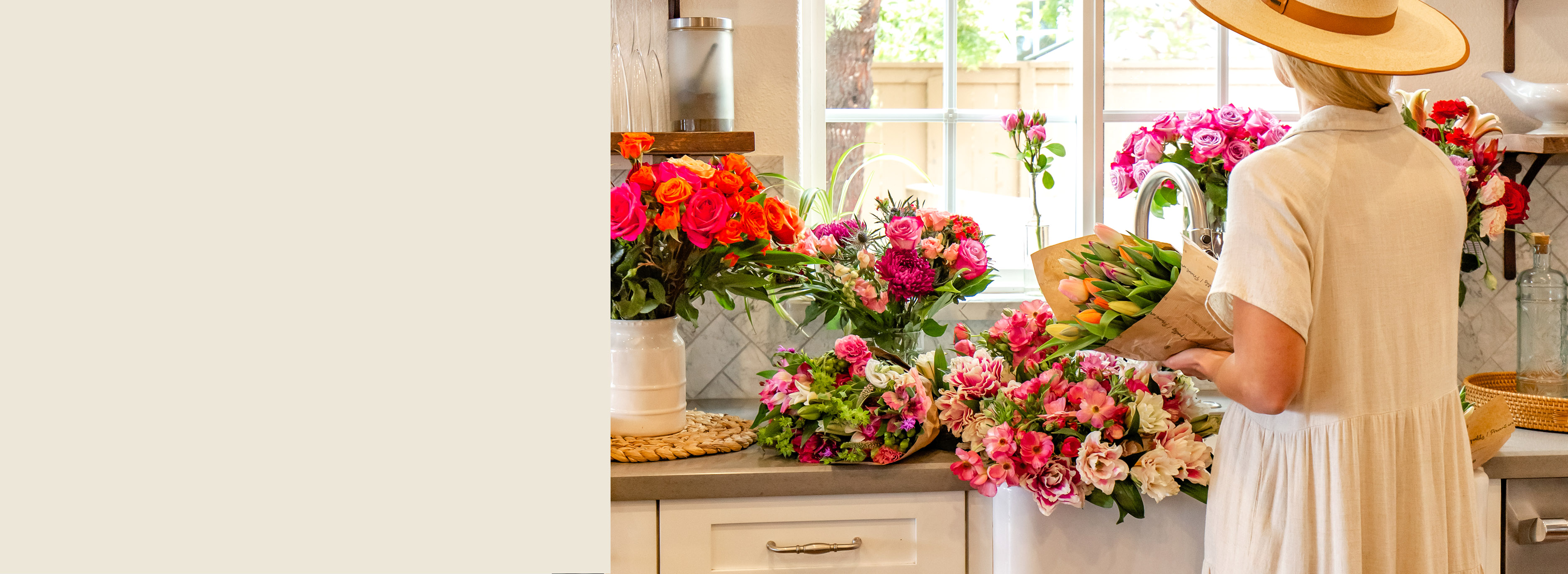 A woman wearing a hat arranges vibrant flower bouquets in a bright kitchen setting.