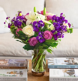 Vibrant mixed flower bouquet featuring purple, pink, and white blooms in a glass vase.