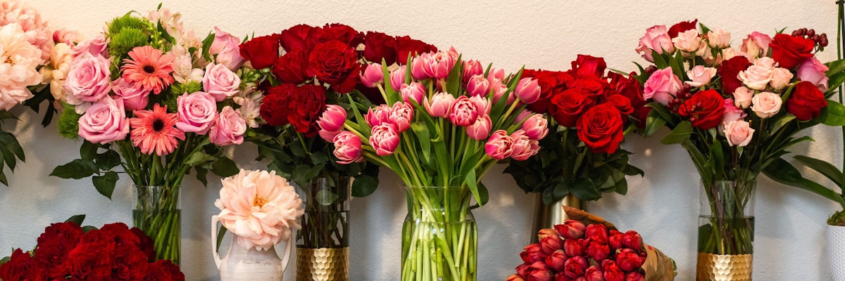 Vibrant floral display featuring red and pink roses, tulips, and daisies in elegant vases.