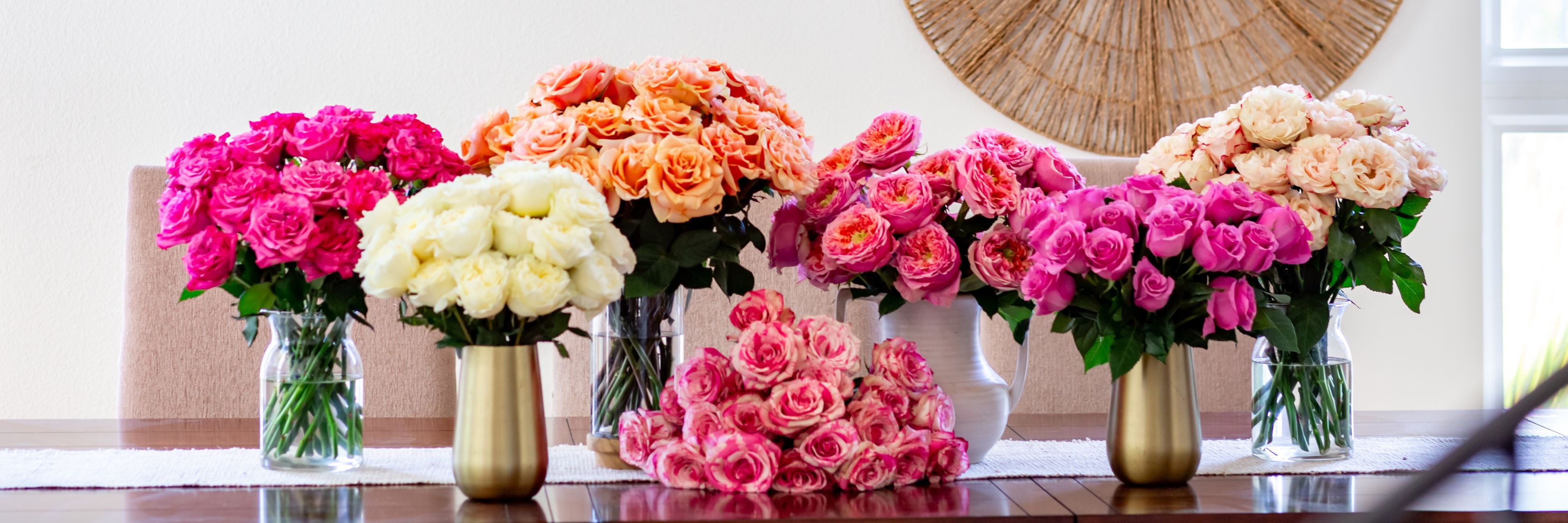 Vibrant floral display featuring pink, orange, and white roses in elegant vases on a table.