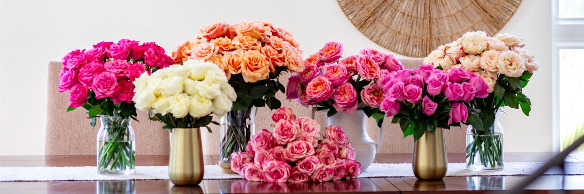 Vibrant floral display featuring pink, orange, and white roses in elegant vases on a table.