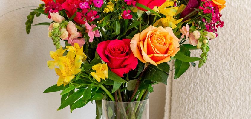 Bright and vibrant floral arrangement featuring roses, lilies, and seasonal blooms in a glass vase.