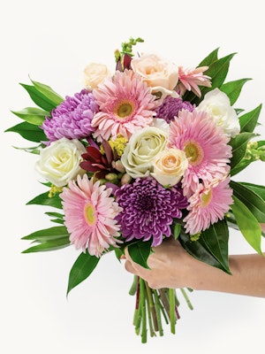 Vibrant spring bouquet featuring pink gerbera daisies, purple flowers, and lush greenery.